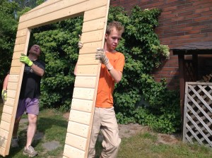 Kaksi miestä kantaa puutarhavajan seinäelementtiä