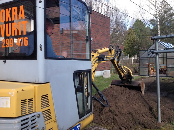 Pieni kaivinkone kaivaa polkua puutarhaan