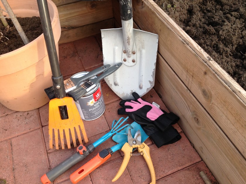 Puutarhatyökaluja, lapio, harava, puutarhasakset, hara. Lisäksi puuöljypurkki ja siveltimiä.