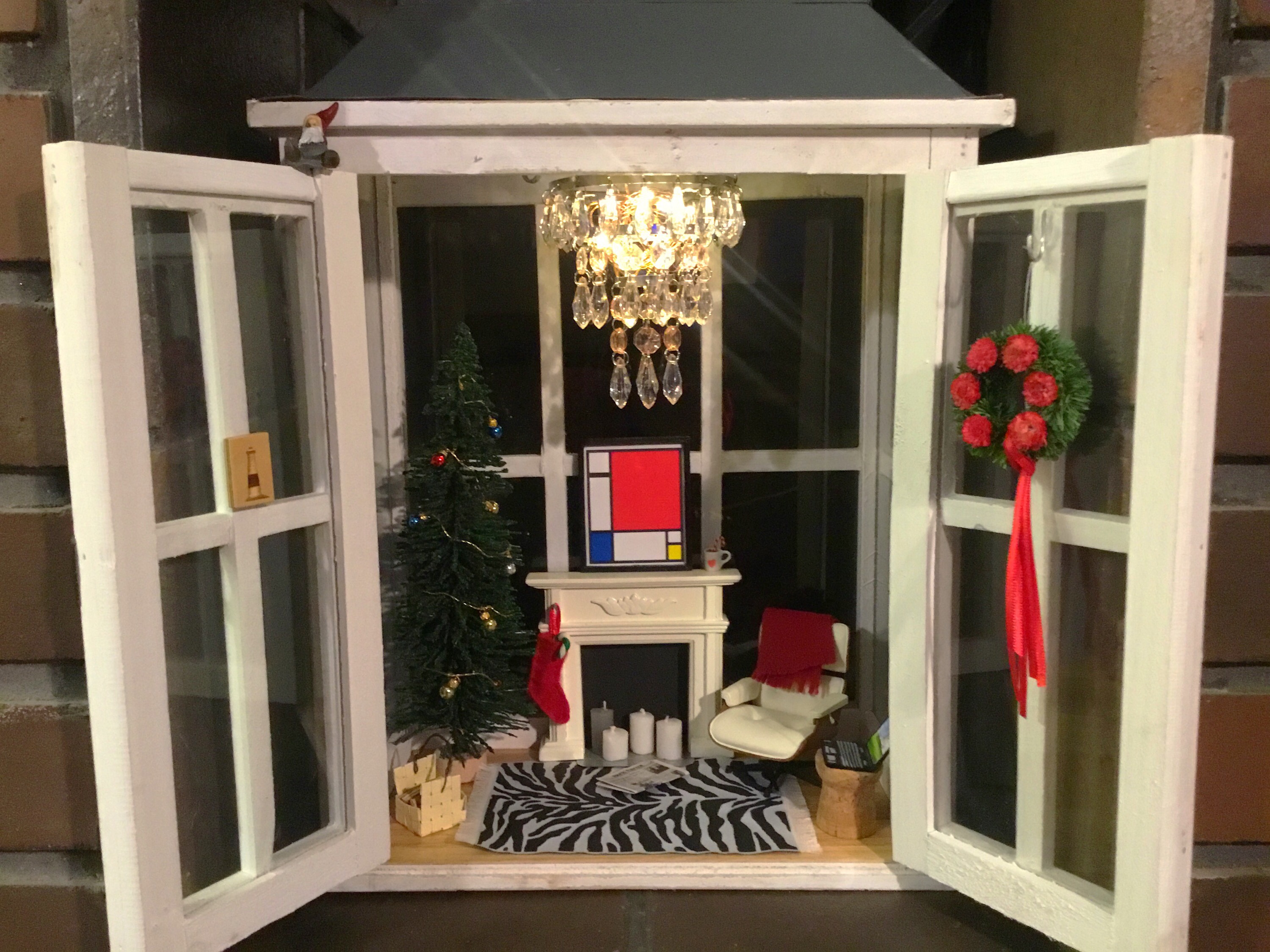 Isoon lyhtyyn tehty jouluinen nukketalo. Joulukuusi, takka ja nojatuoli.