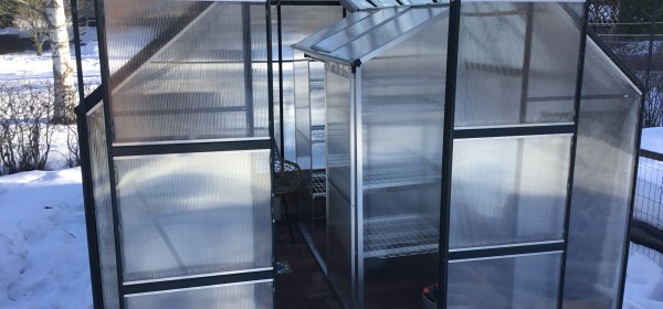 Pieni seinämallinen kasvihuone isomman kasvihuoneen sisällä.