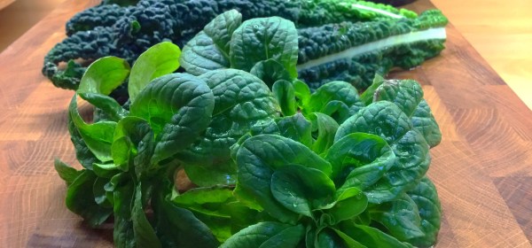 Palmukaalin lehtiä sekä muutama pieni salaattivuonankaali leikkuulaudalla.