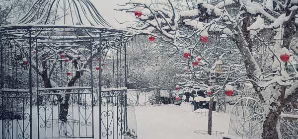 Metallinen puutarhapaviljonki lumisessa puutarhassa.