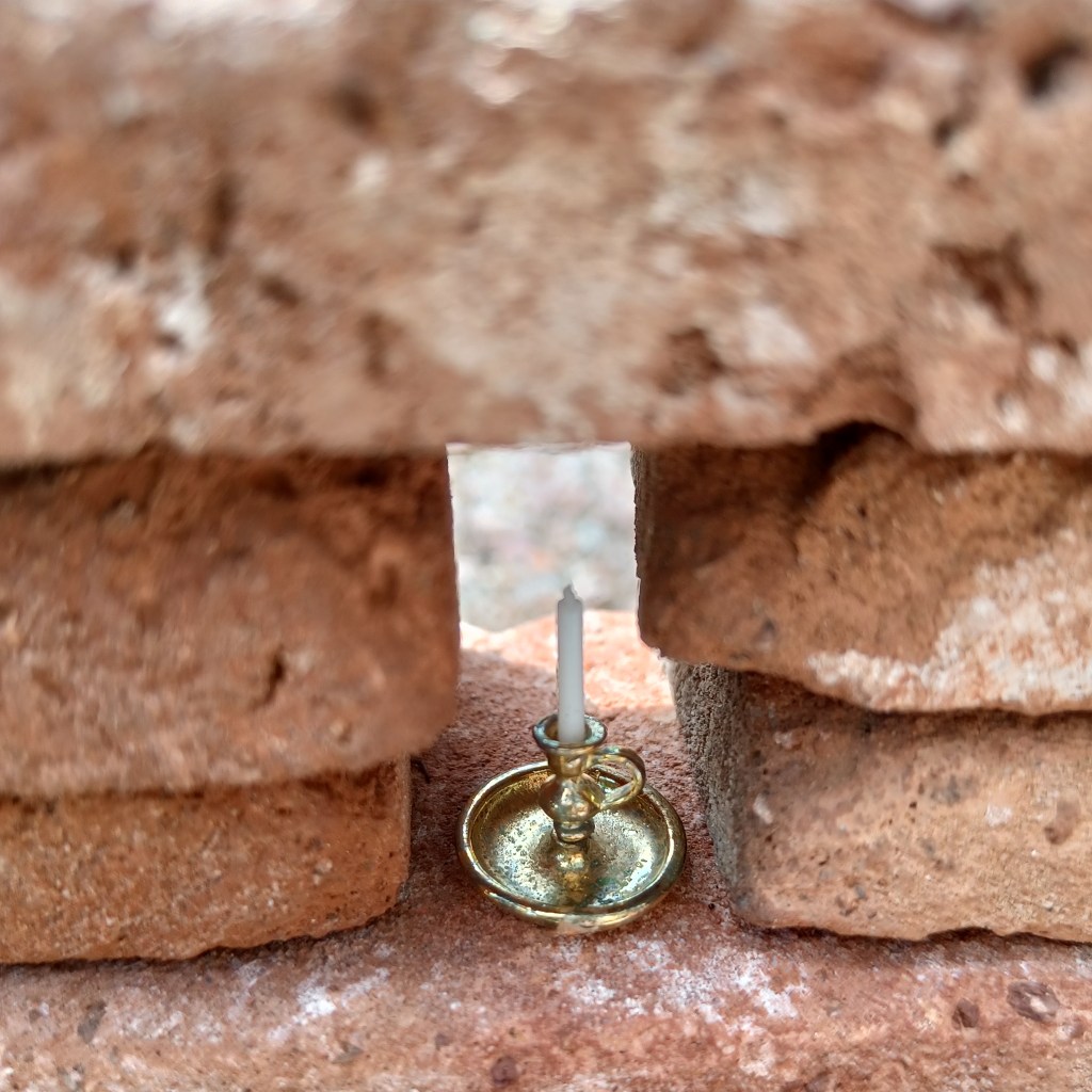 Yksityiskohta keijupuutarhasta: kynttilä omassa kolossaan muurin keskellä.