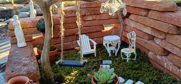 Laattatiilistä keijuille koottu puutarha, jossa keinu, istuinryhmä, veistoksia ja ruukkuja.