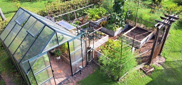 Ylhäältä otettu kuva omakotitalon puutarhan kasvihuoneesta ja kasvimaasta.